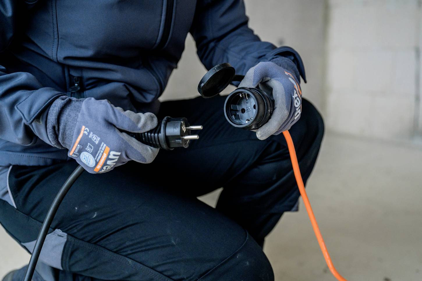 A person wearing gloves is holding two connectors, ready to connect an orange cable.