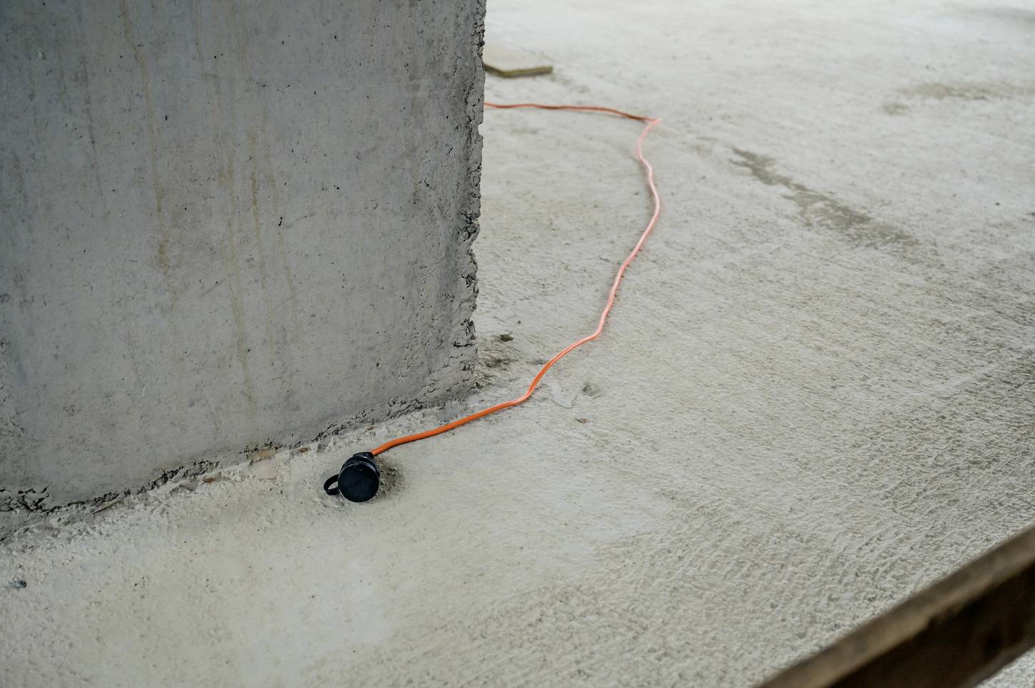 An orange extension lead runs across a concrete floor next to an unfinished concrete wall.