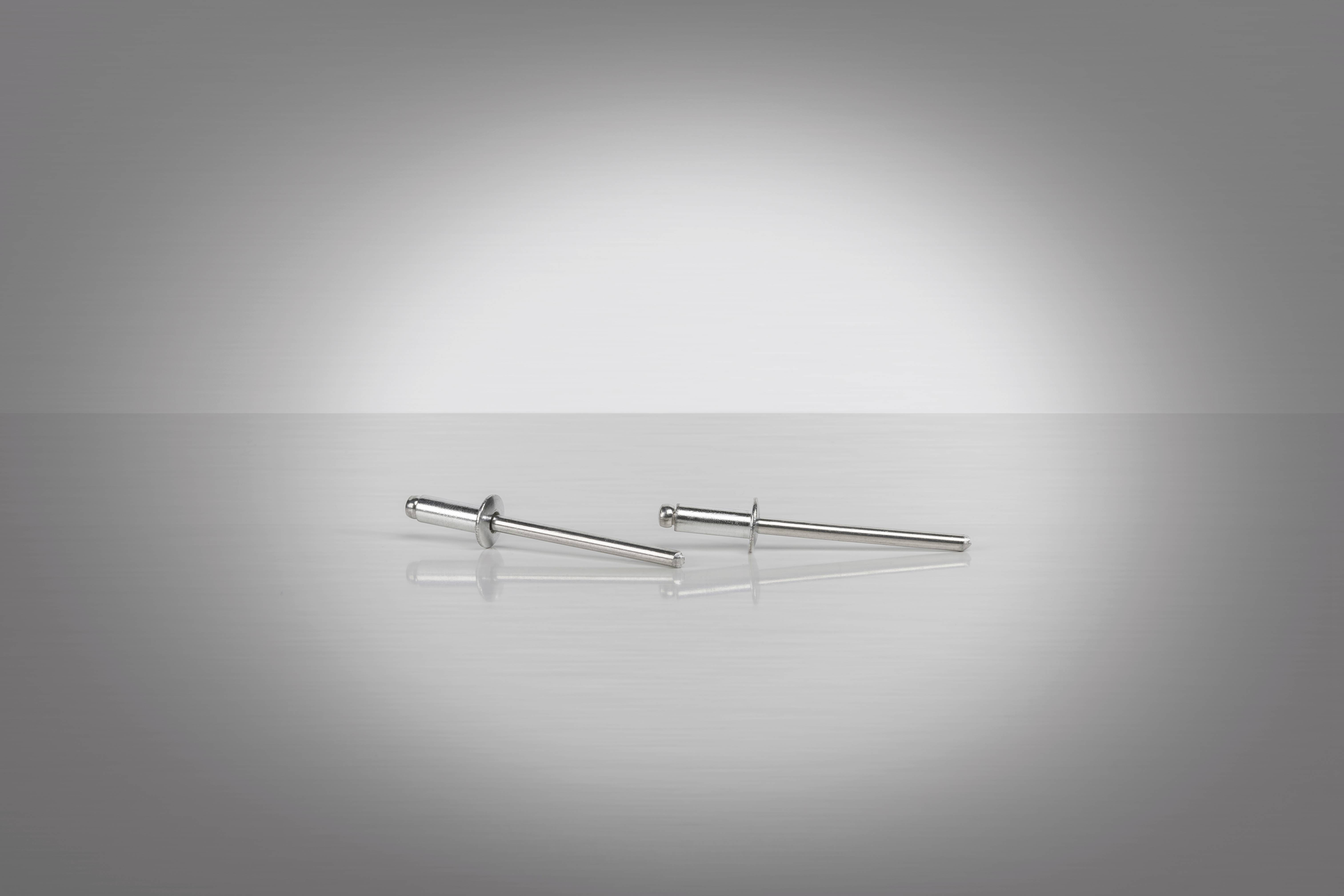 Two silver rivets on a reflective surface, lying in the light against a grey background.