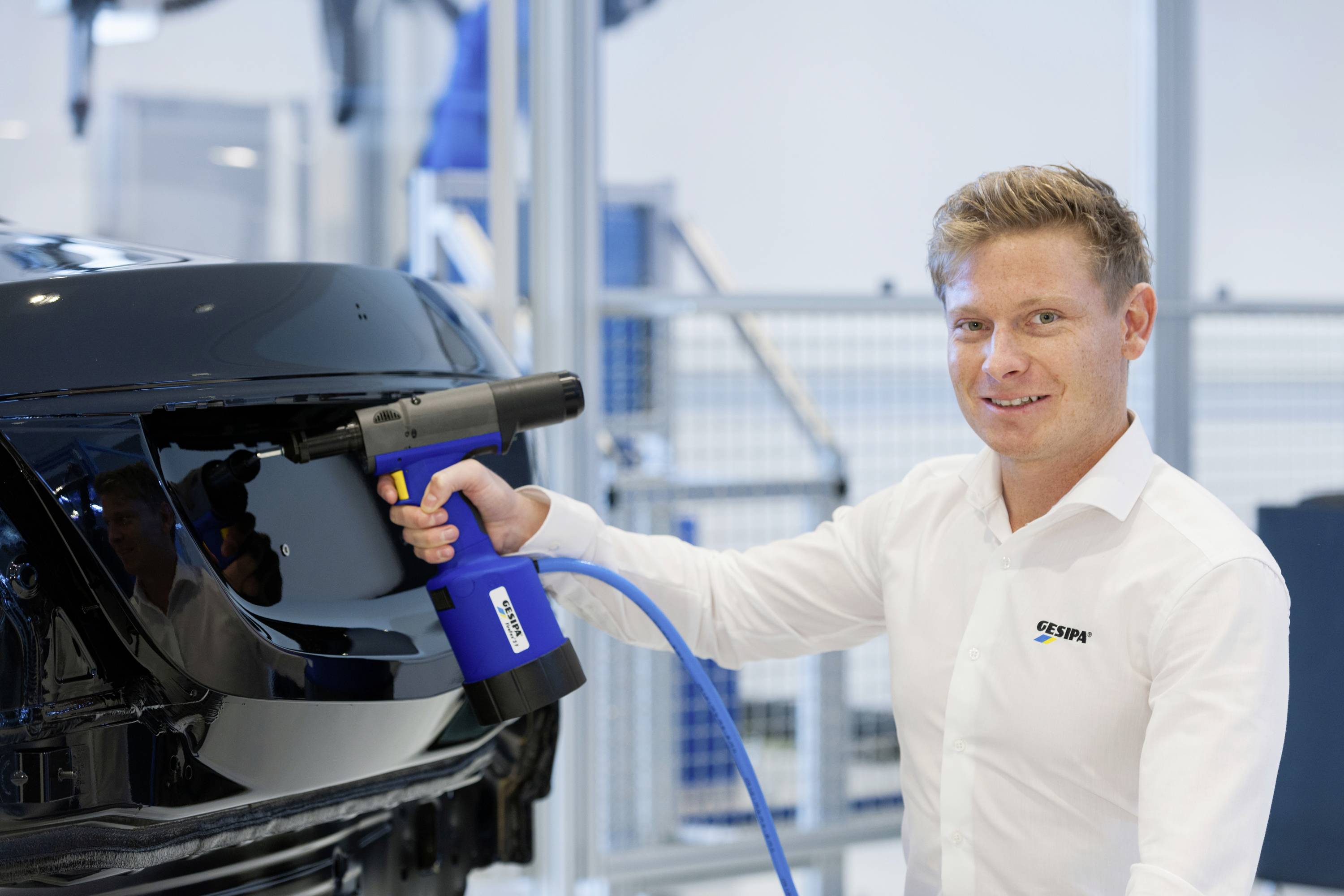 A man in a white shirt is using an electric tool to work on the surface of a glossy black automotive part.