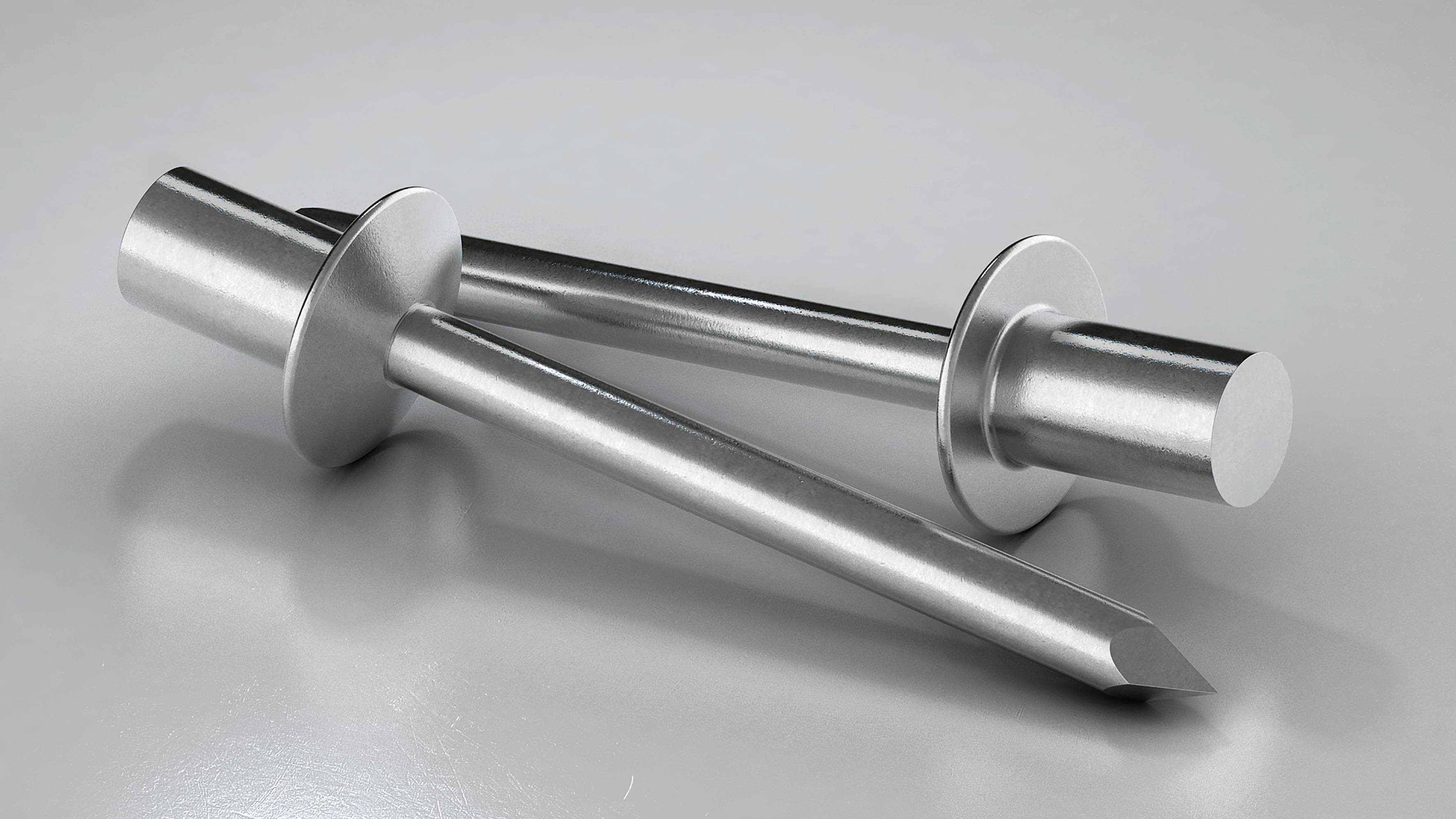 Two silver metal stamps with flat and pointed ends are crossed over each other on a smooth, reflective surface.