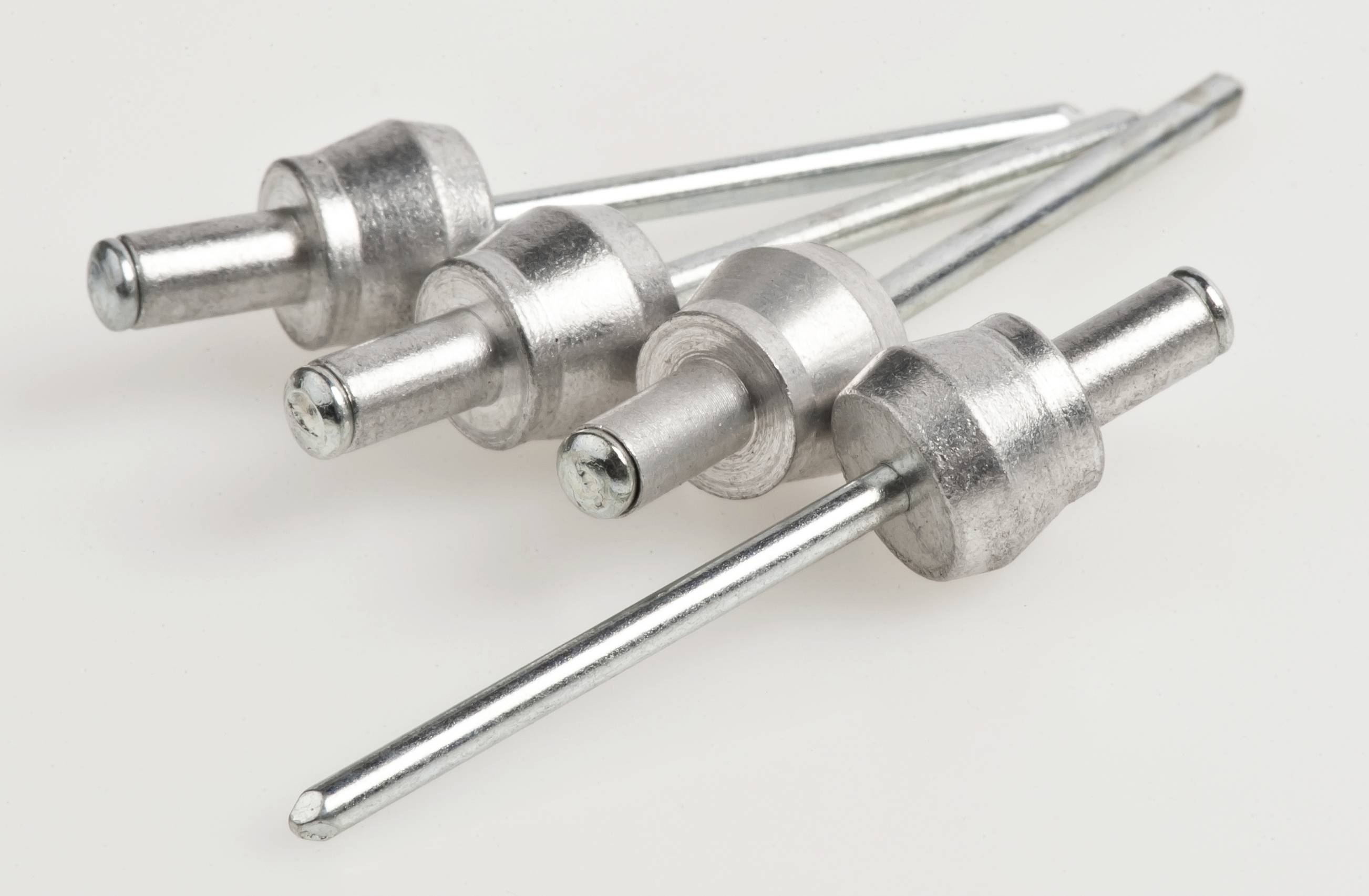 Four silver blind rivets on a light background, arranged in a diagonal line.