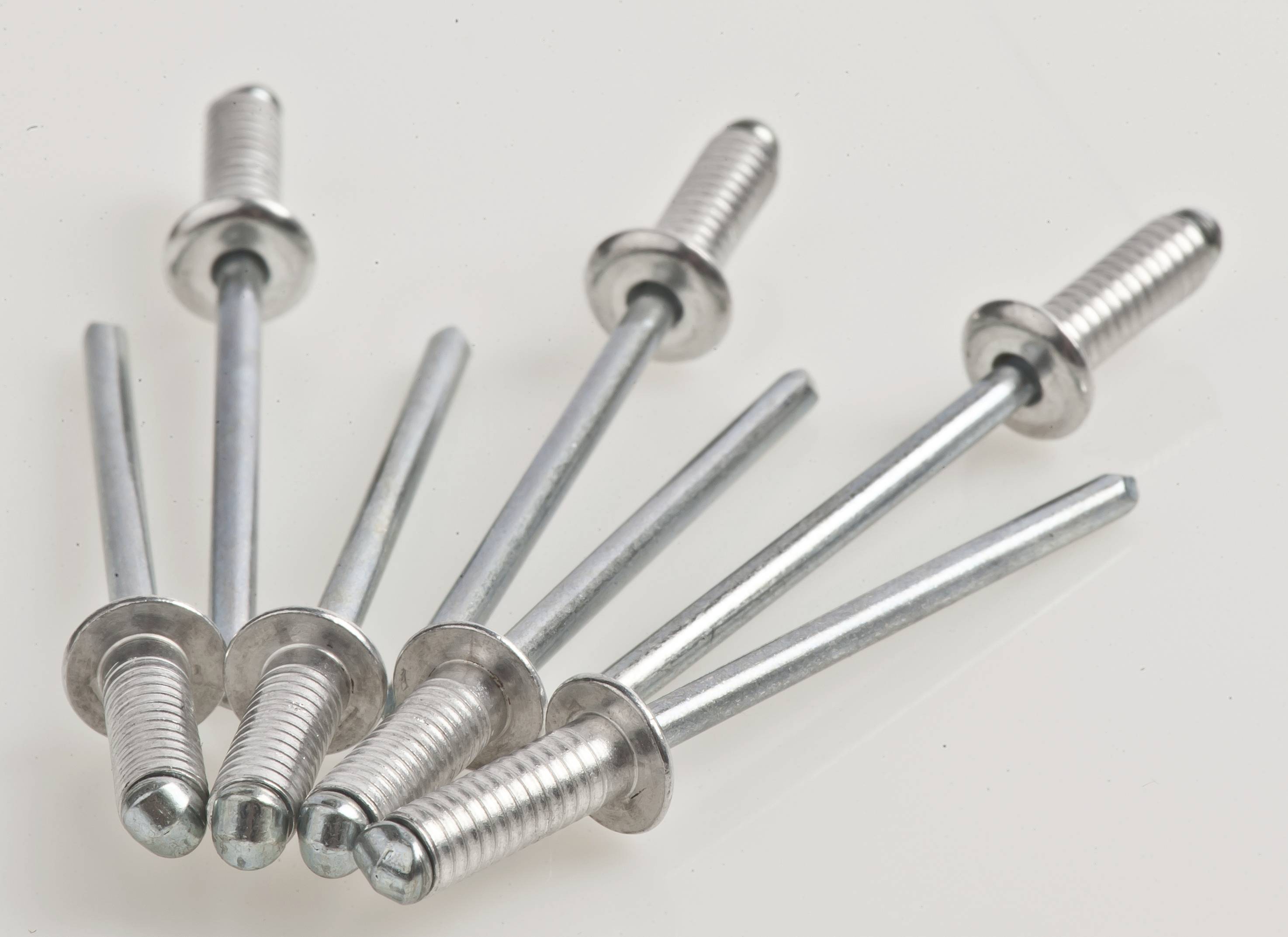 Six silver blind rivets are arranged in a fan-like pattern on a white surface.