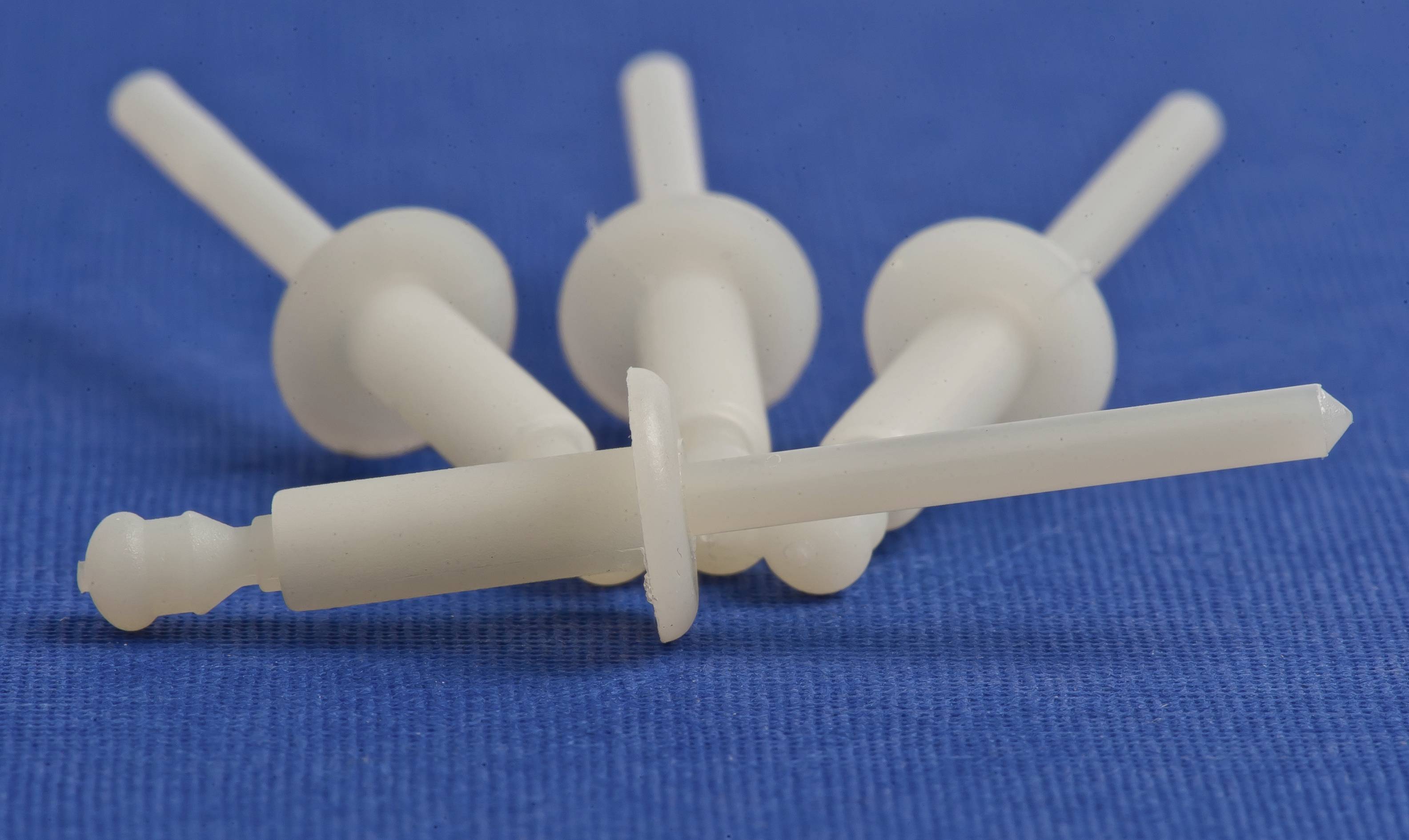 Four white wall plugs are lying on a blue cloth, arranged in a fan-like pattern.