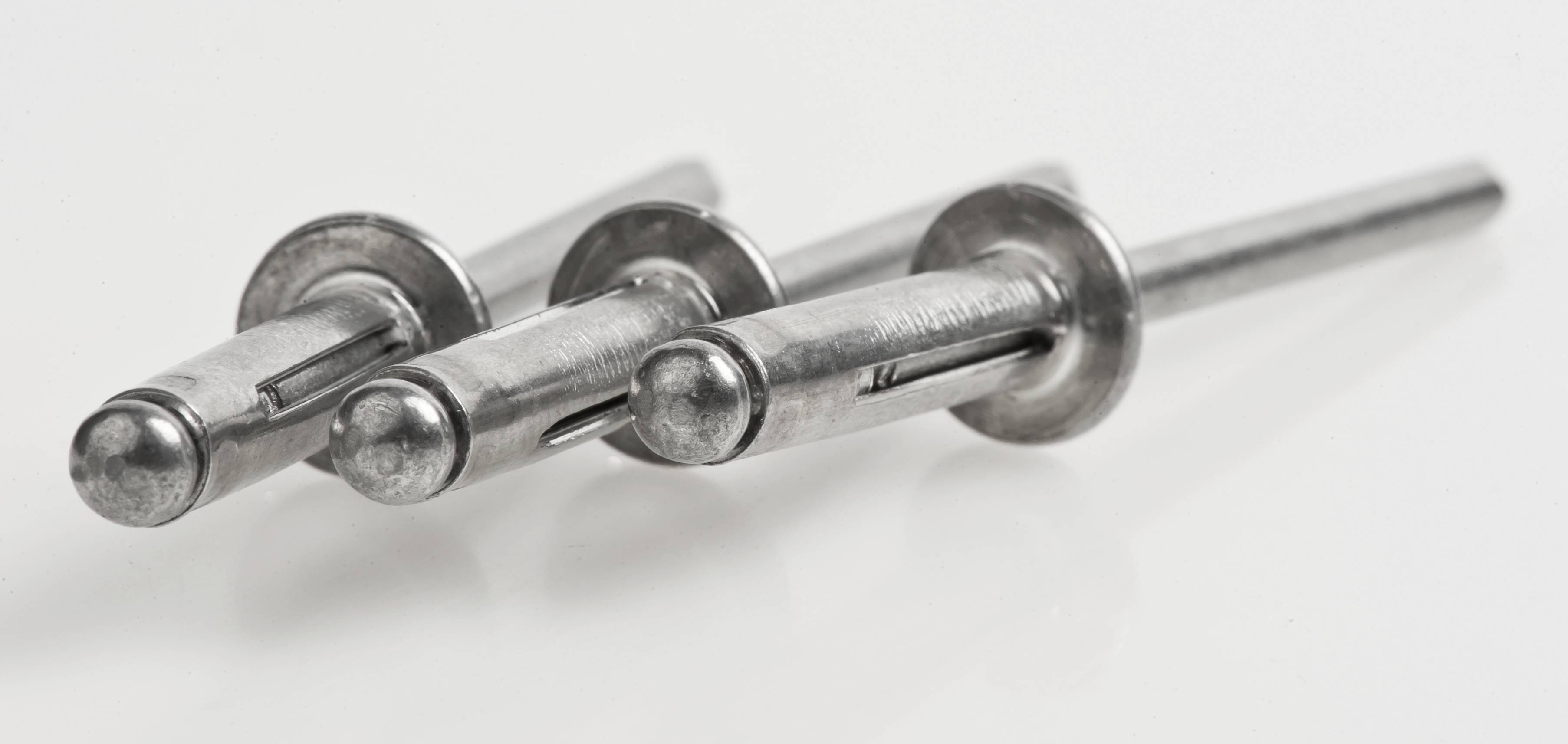 Three aluminium pop rivets on a white background, arranged diagonally. They have shiny surfaces and rounded heads.