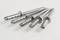 Metallic nail plugs on a white background, arranged diagonally, display their ribbed shafts.