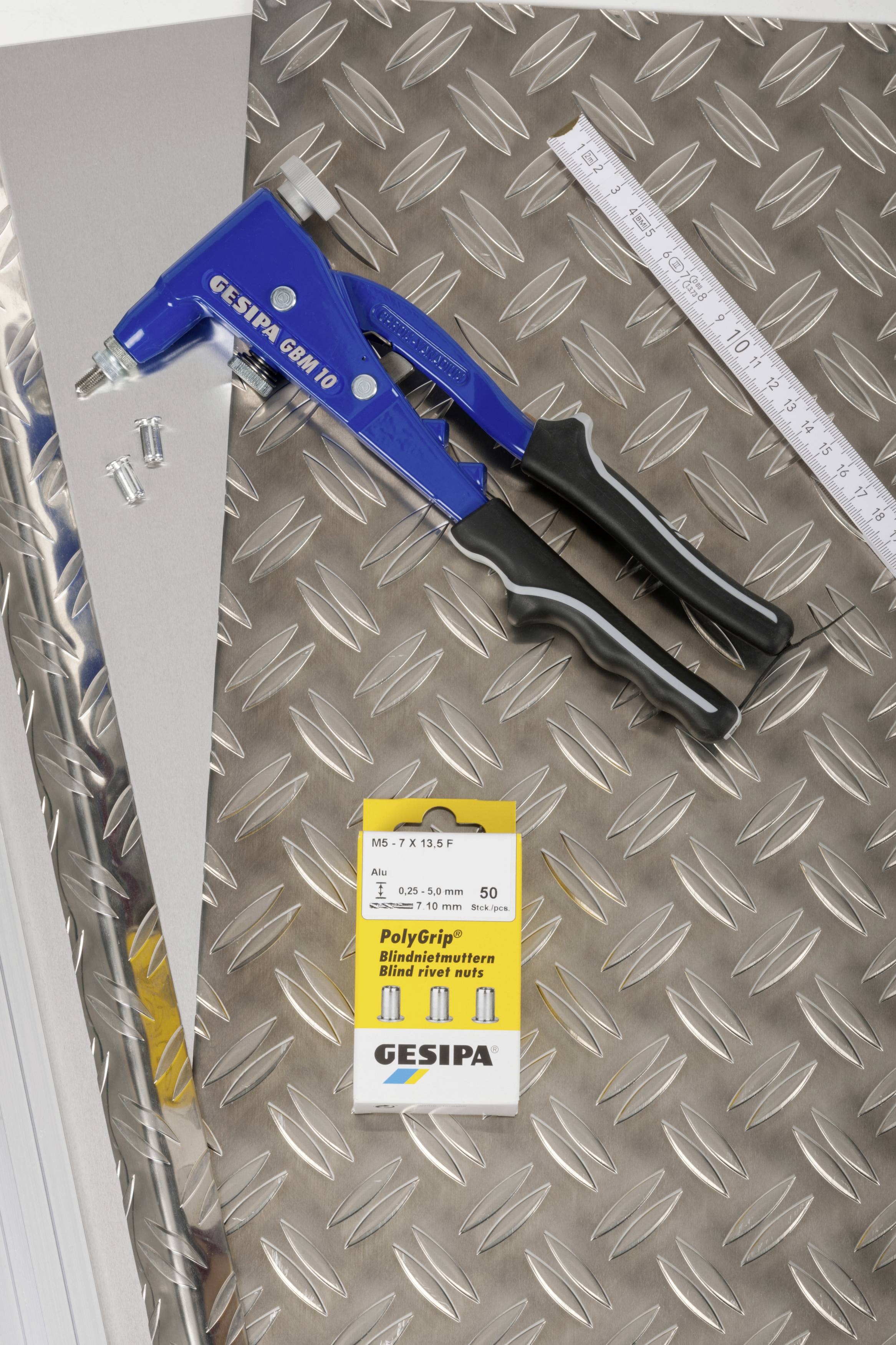 A blue blind riveting pliers lies on a textured metal surface, alongside a pack of rivets and a ruler.
