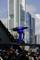 A blue shooting device stands on a railing covered in love locks, with modern skyscrapers in the background.