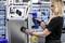 A woman is wearing safety glasses and gloves while using a blue electric tool to work on a silver cabinet.