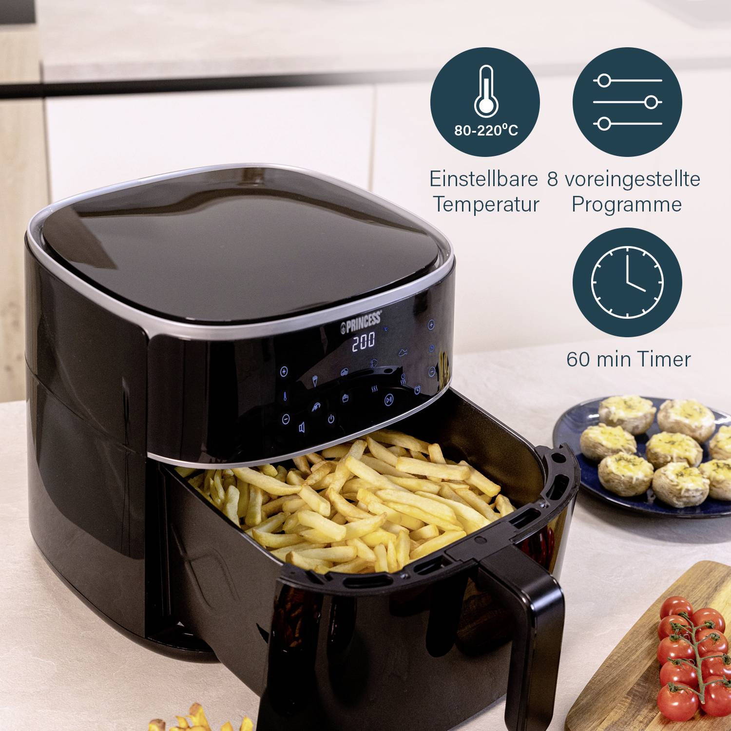 A black air fryer with LED display is frying chips. Symbols show: '80-220°C', '8 Programmes', '60 min Timer'. In the background, stuffed mushrooms are visible.