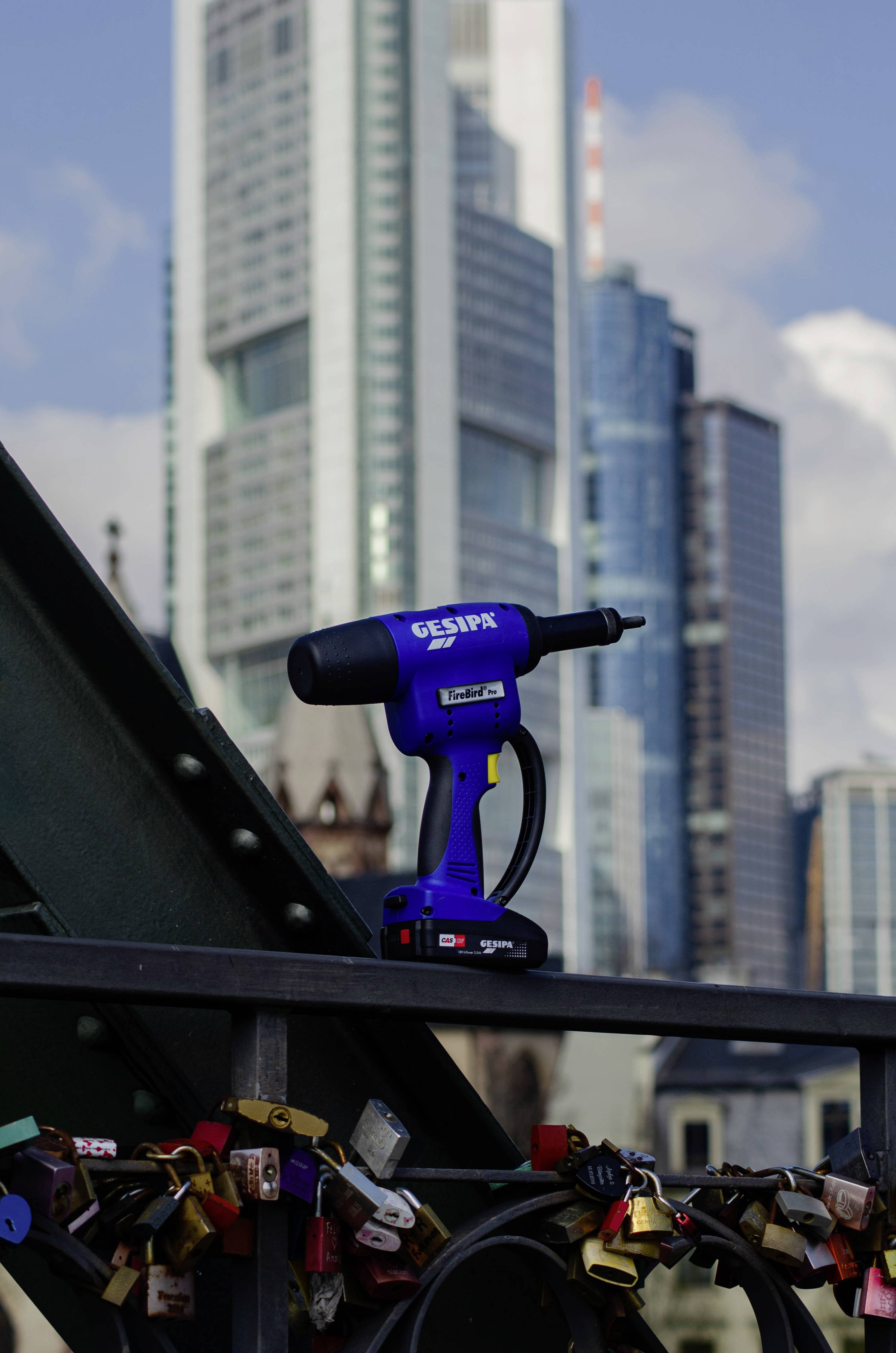 'Rivets tool on bridge, surrounded by padlocks. High-rise buildings in the background, symbolising love and urbanity.'