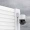 A surveillance camera mounted on a white wall in the rain. The camera is weatherproof and aimed at the exterior area.