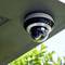 Security camera mounted on the ceiling, surrounded by green leaves in the background, symbol of security and surveillance.