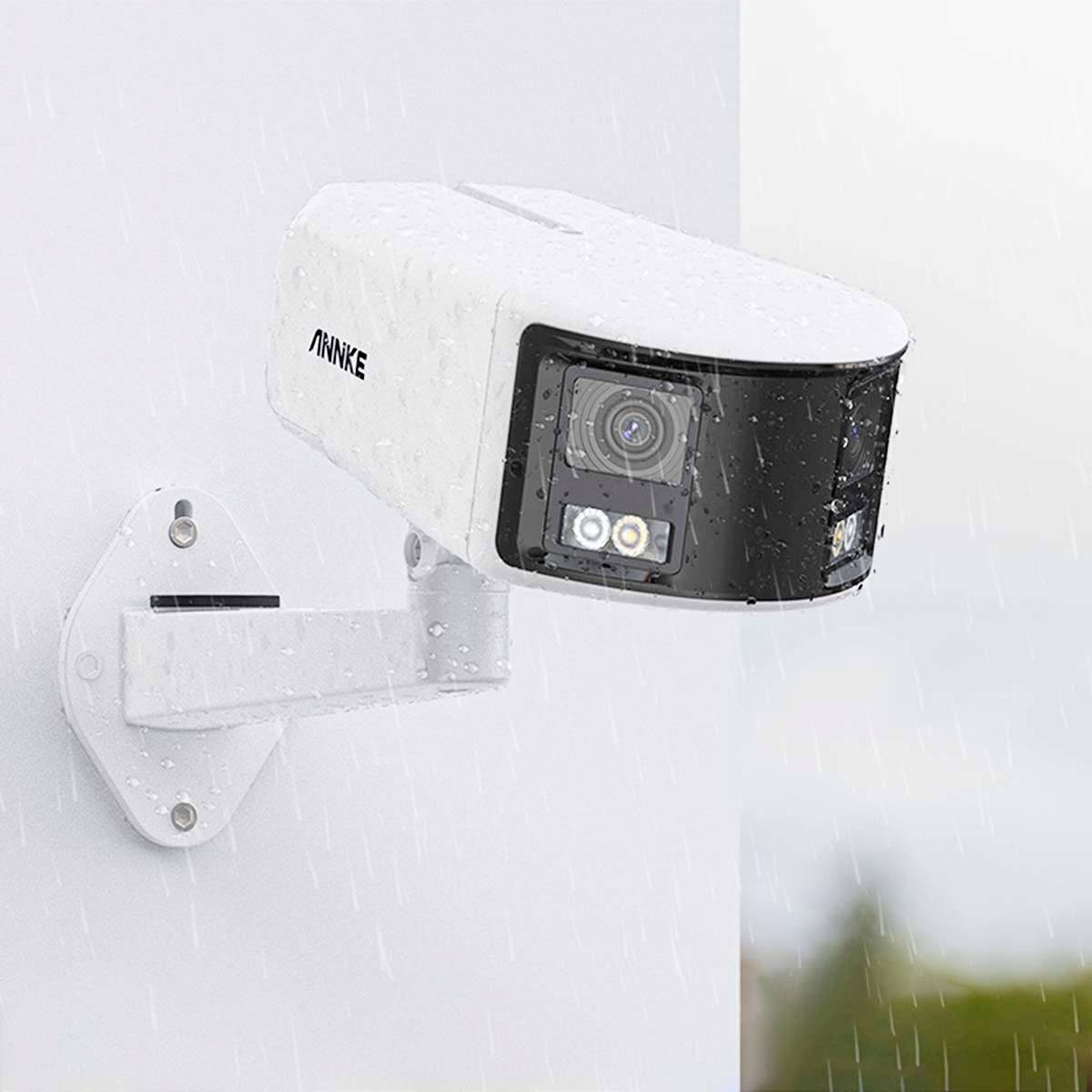 A white surveillance camera by ANNKE is mounted on a wall in the rain. It has infrared LEDs and a motion sensor.