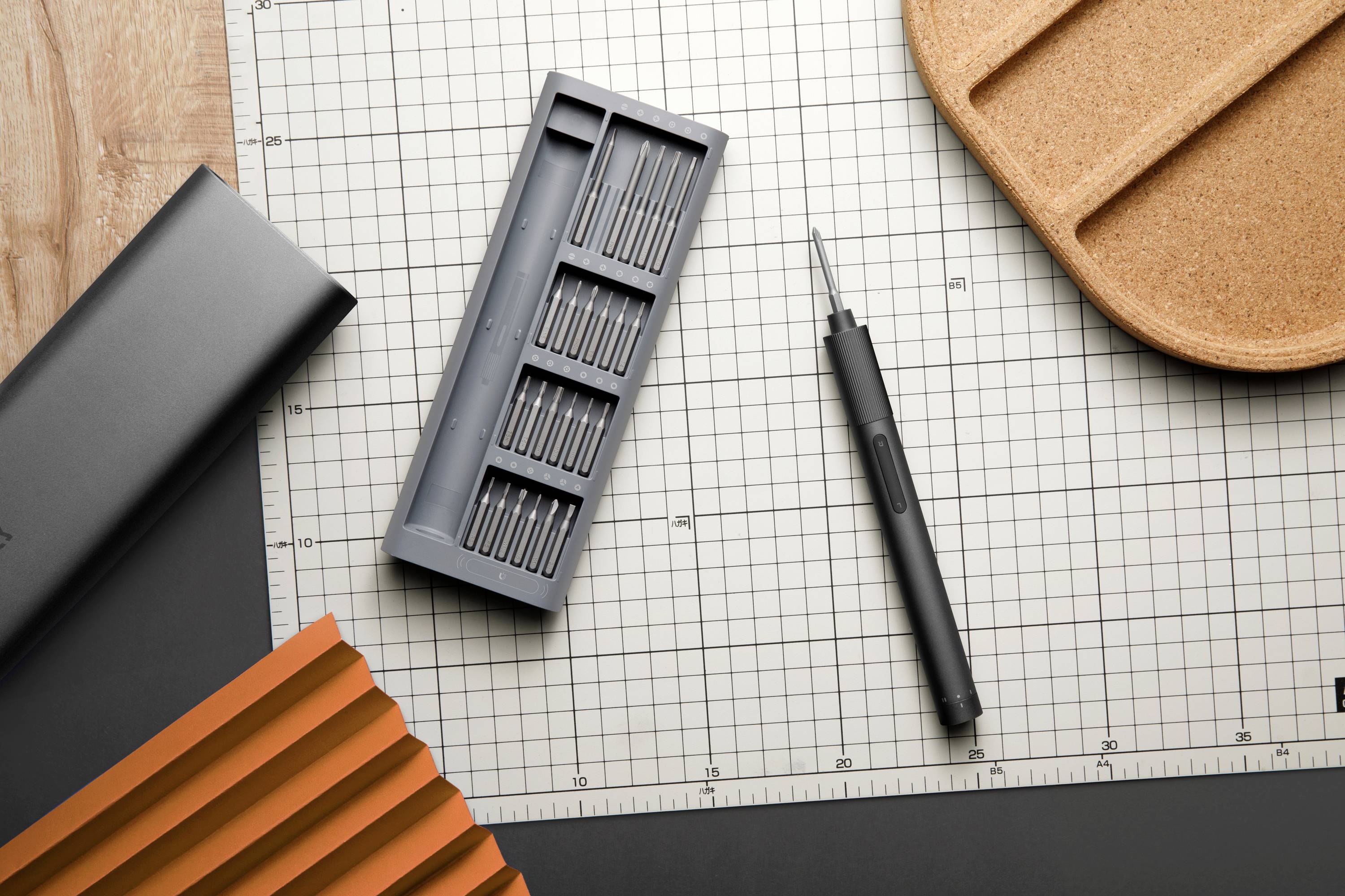 Tool set on a checked background. Includes a magnetic screwdriver with various attachments and a brown tray.