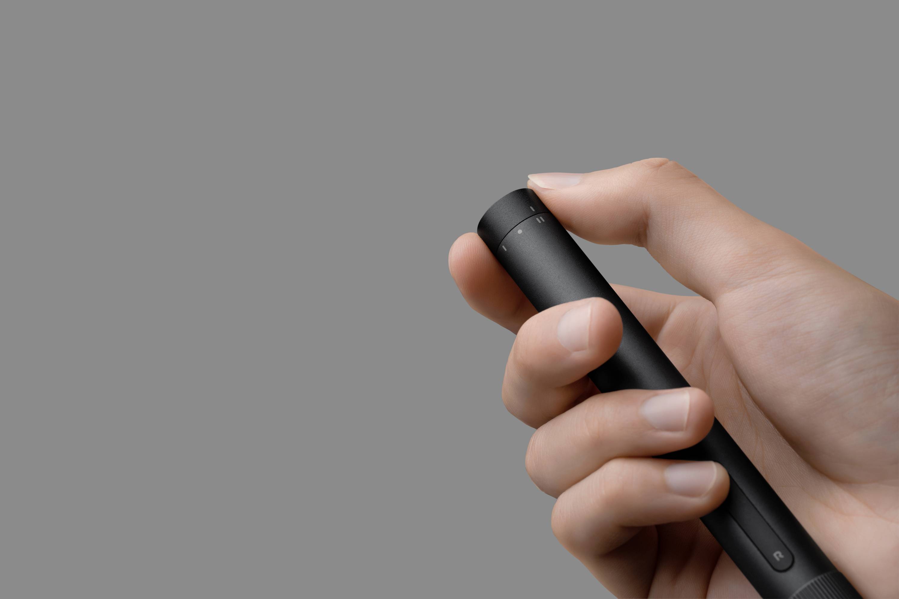 A hand is holding a black pen against a grey background.