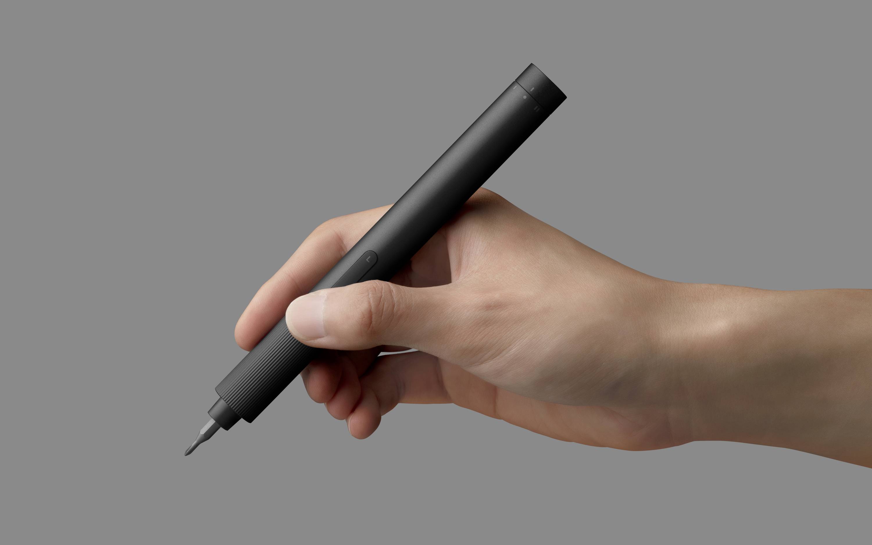 A hand holds a black marker against a grey background.