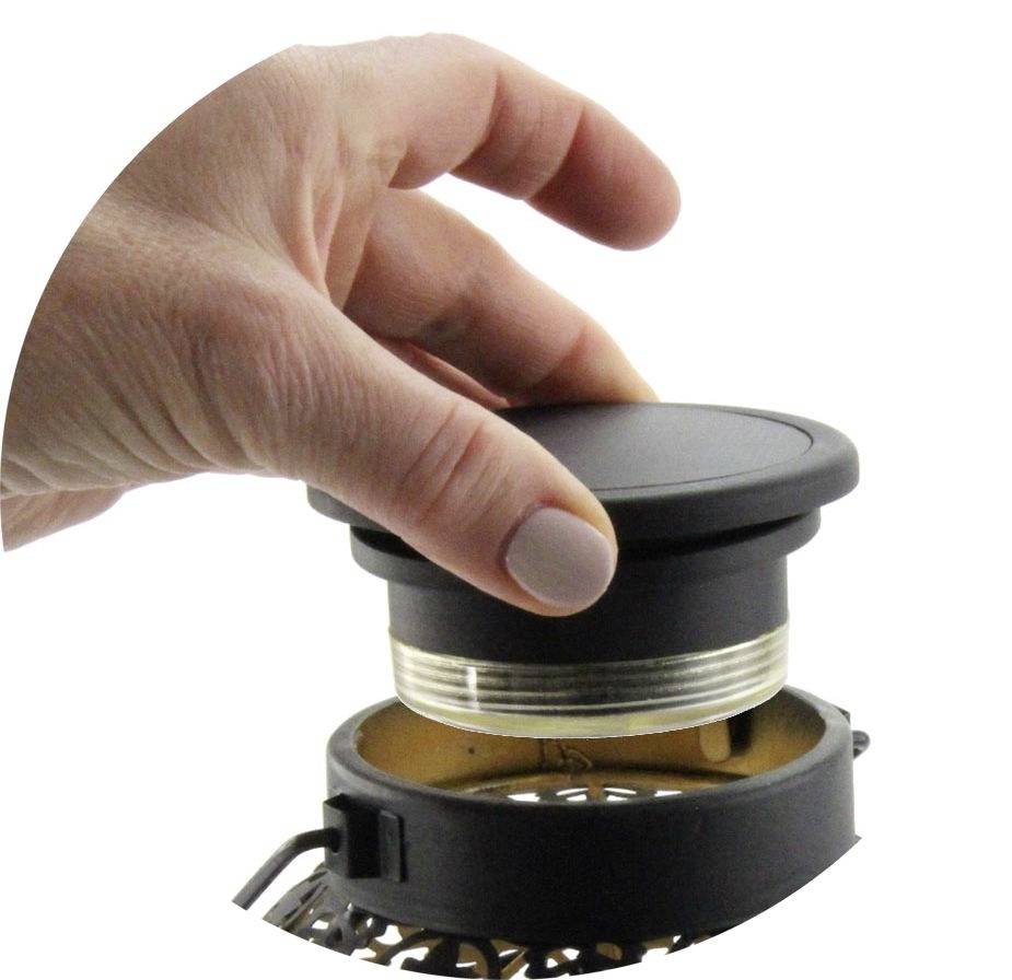'A hand is holding a round black lid over a metal and glass device.'