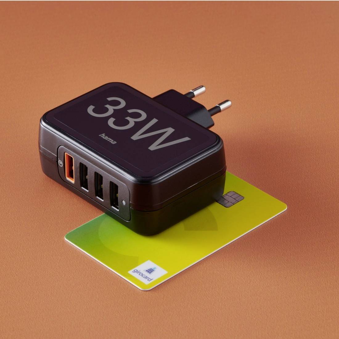 A 33W multi-port USB charger with four ports, including an orange fast-charging port, lies on a card.