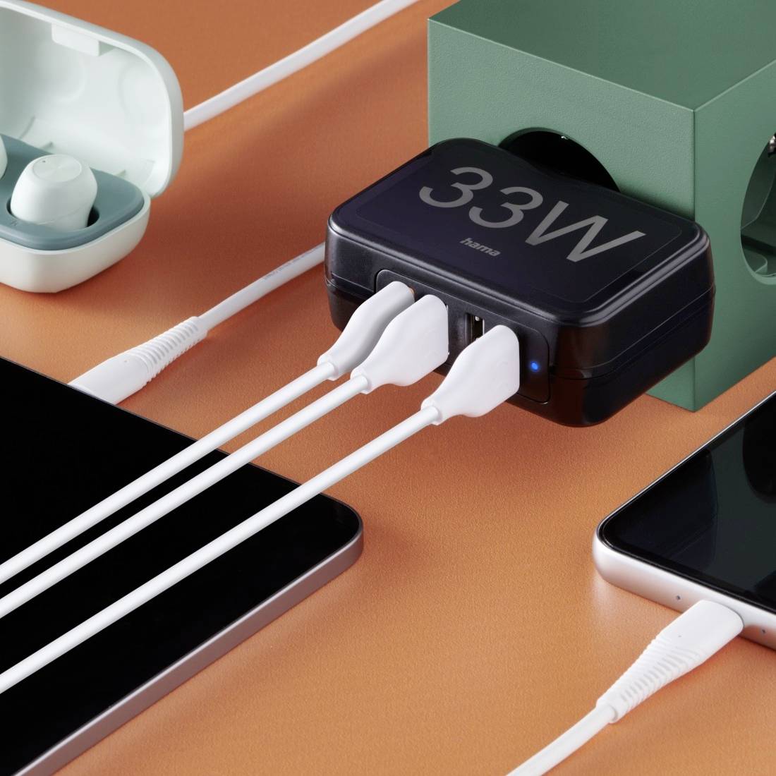 A charger with three connected cables displays '33W'. Wireless earbuds and a smartphone are visible in the background.