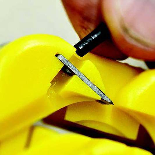 Close-up of a hand operating a pencil sharpener. The pencil is being sharpened, with shavings visible.