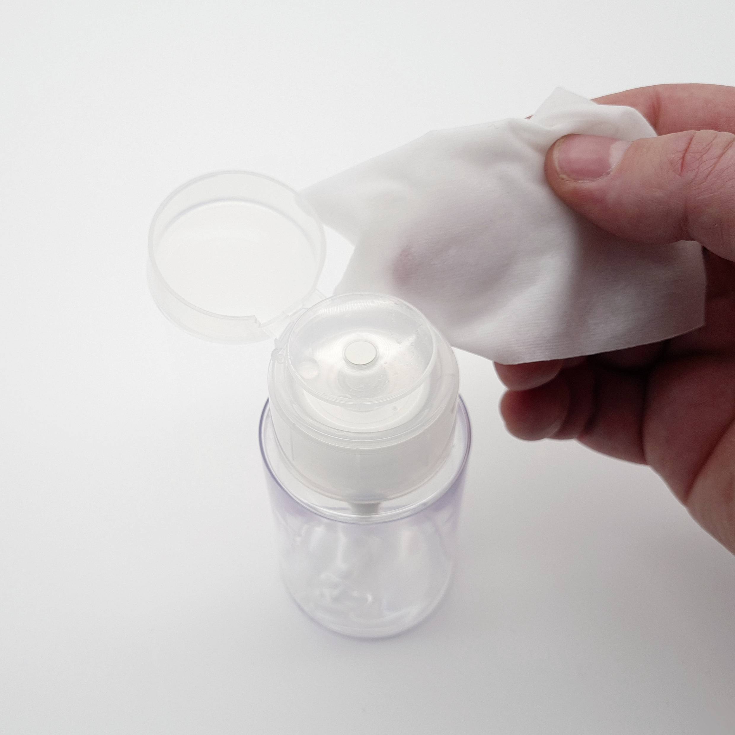A hand is holding a cotton pad and pressing it against the opening of a pump dispenser to absorb liquid.