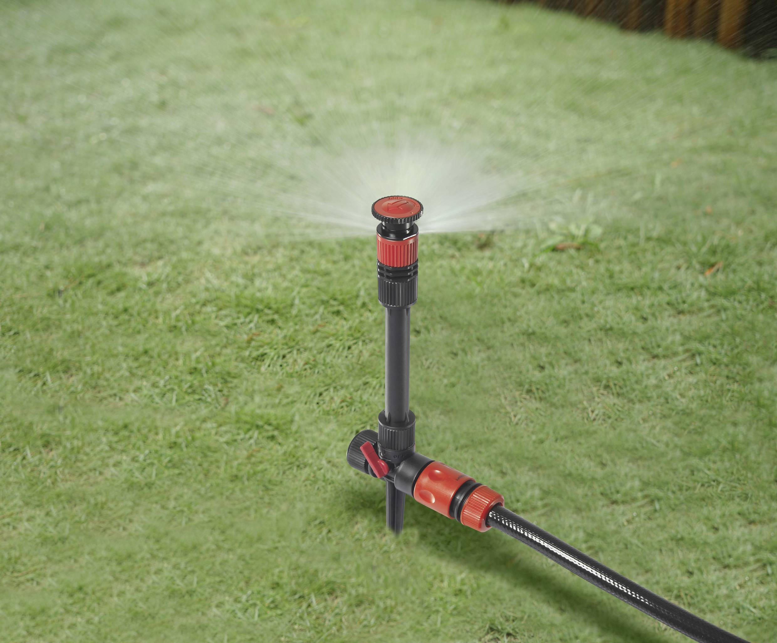 Lawn sprinkler on green grass distributes water in a circular motion.
