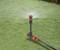 Lawn sprinkler on green grass distributes water in a circular motion.