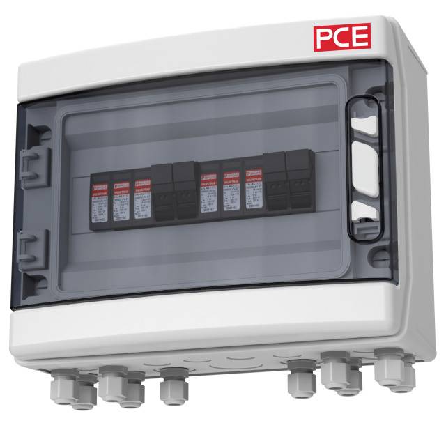 An electrical distribution board with a transparent lid reveals several circuit boards inside. The red 'PCE' logo is positioned in the top right corner.