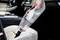 A person is vacuuming the seat of a car with a small, cordless handheld vacuum cleaner. The seat is made of white leather.