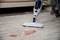 Steam cleaner removes red stain from wooden floor. Sofa and person blurred in the background. Focus on cleaning process.