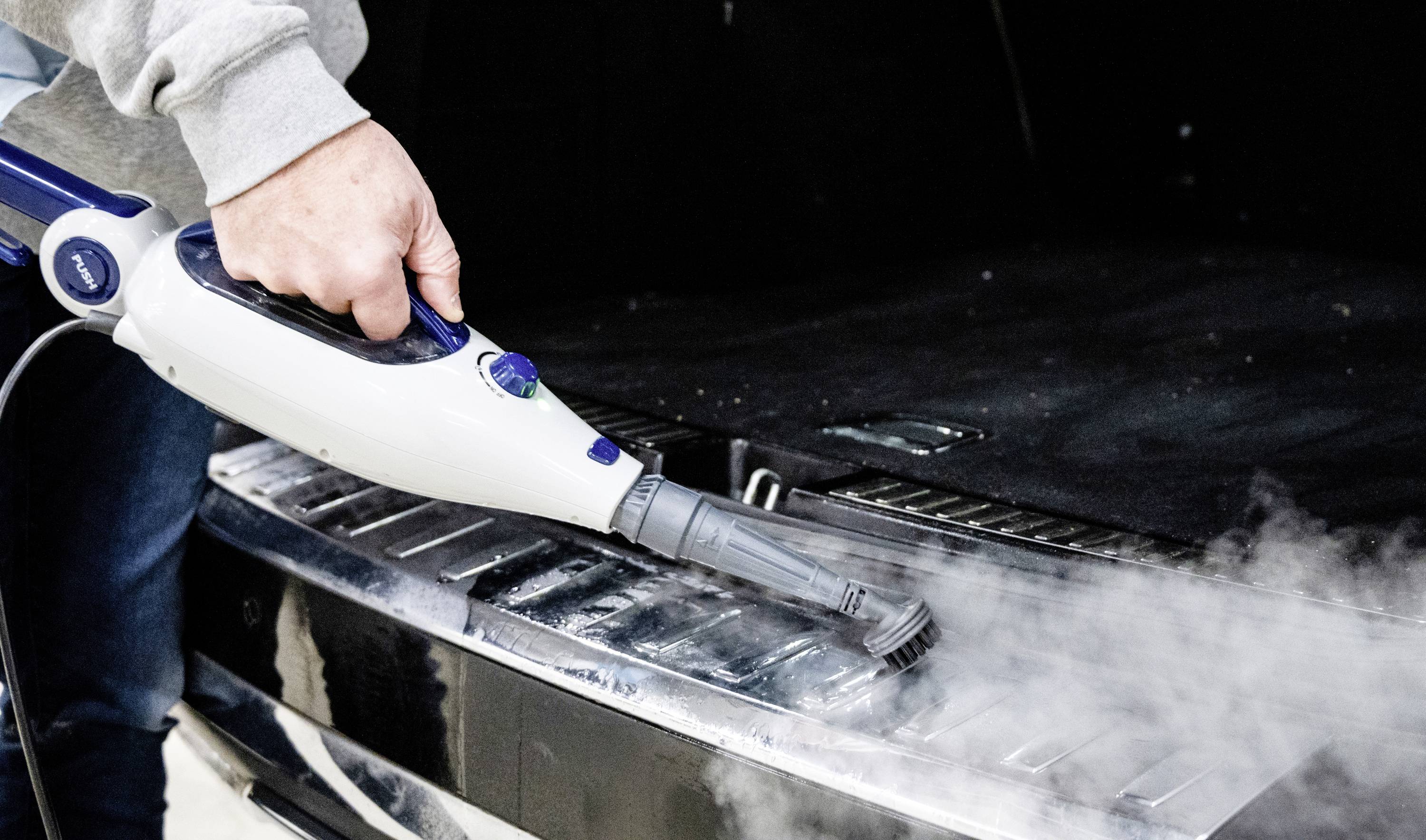 A person is cleaning the boot of a car with a steam cleaner.