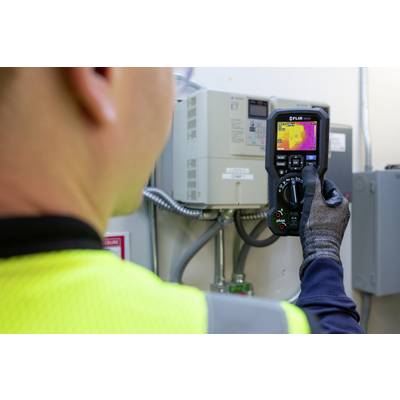 A person in safety clothing is using a thermal imaging camera to check the temperature of an electrical device.