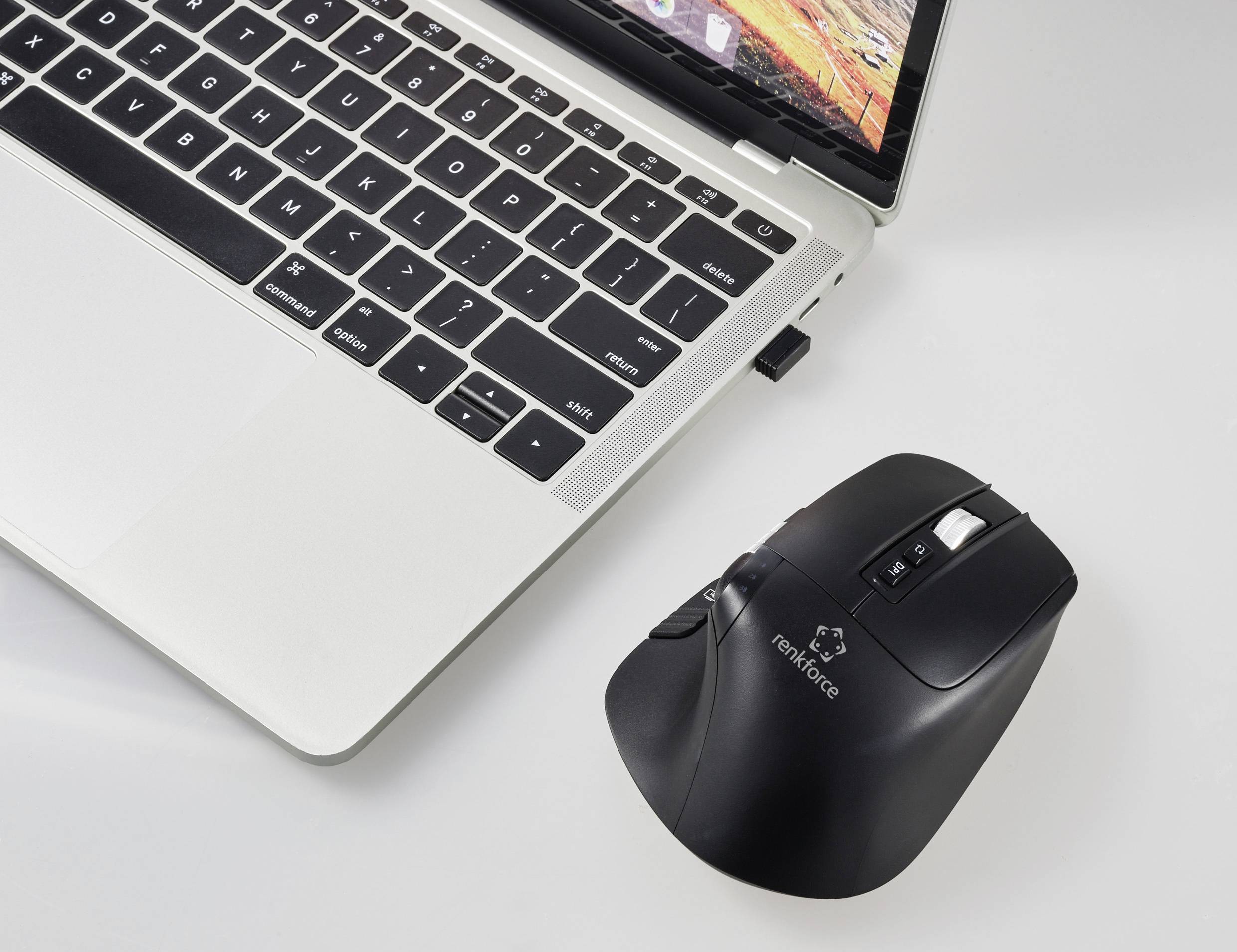 A laptop with its lid open and an illuminated keyboard sits on a white table. Beside it lies a black wireless mouse.