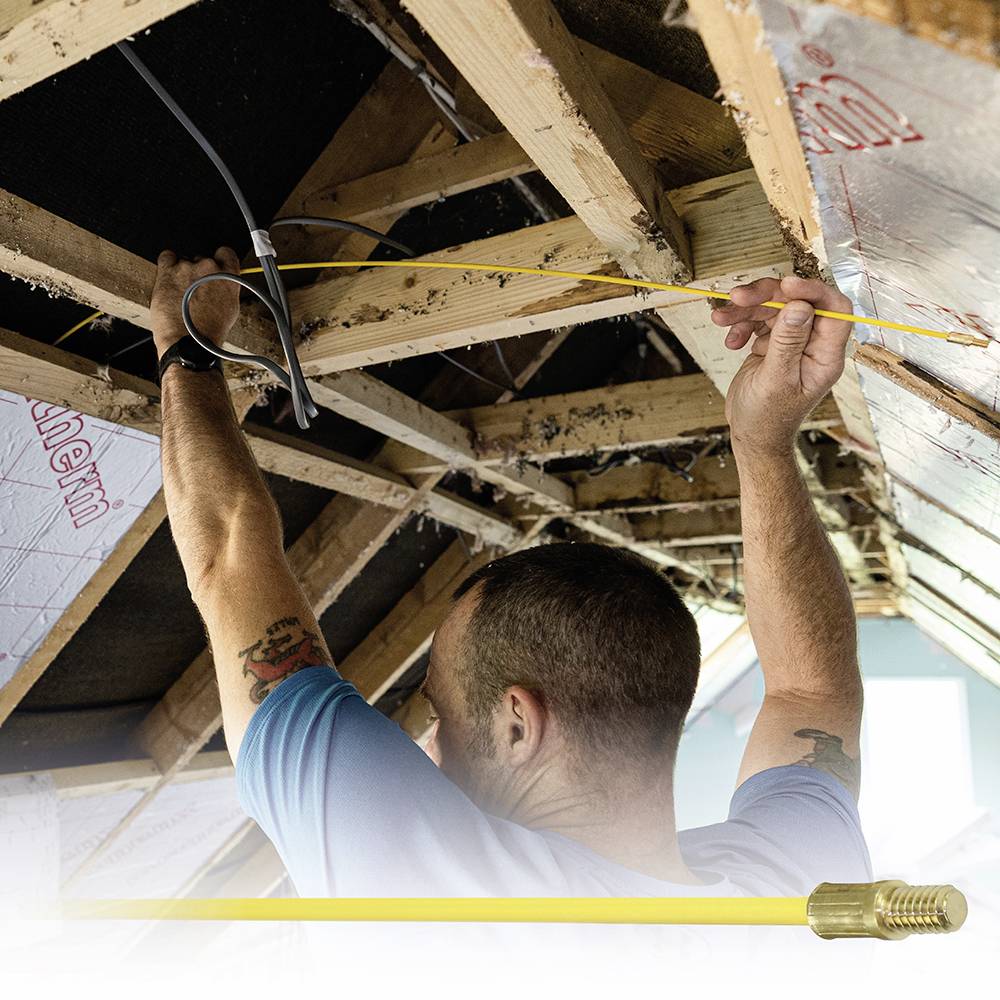 A person is installing a thermostat cable on an exposed roof truss, surrounded by insulation material. Below is a close-up image of a cable connection.