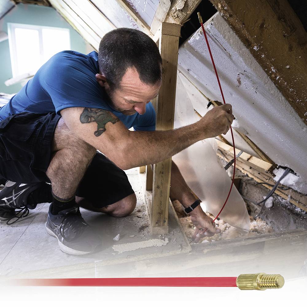 A man is repairing the insulation of an attic. He is wearing a blue shirt and using a red cable to carry out the work.