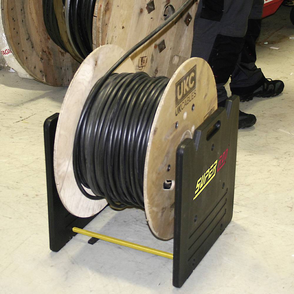 A large cable drum on a roller stand in the warehouse. Another cable lies in the background. A person is standing beside it.