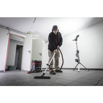 A person is vacuuming the floor in an empty room with an industrial vacuum cleaner. An open door is visible in the background.