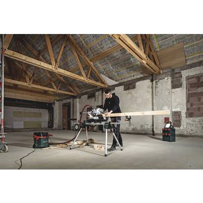 A person is working with a table saw in what initially appears to be an empty room, cutting through a wooden beam. A wooden beam ceiling is visible.