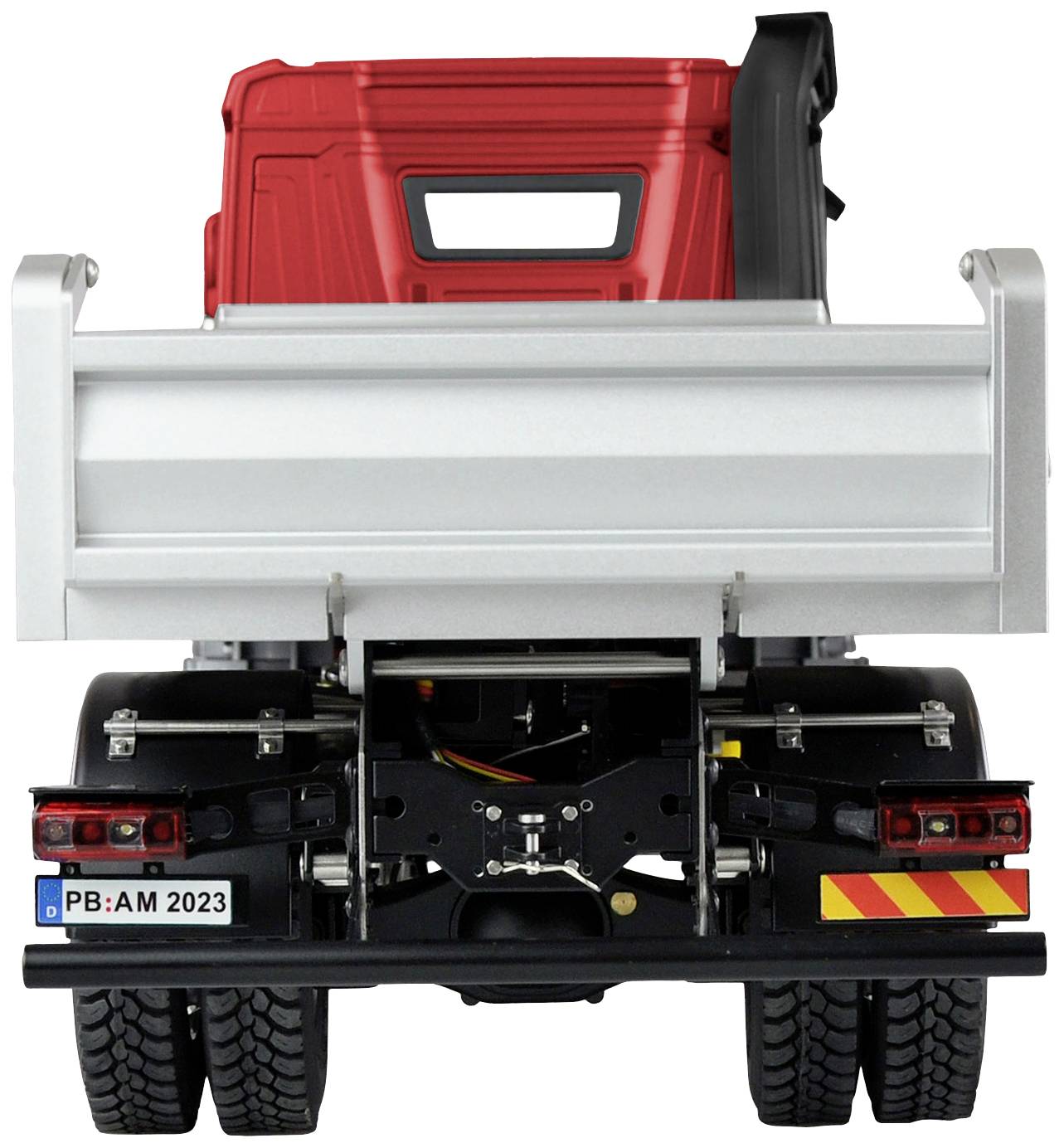 A tipper truck, photographed from behind, with a red cab and silver loading area. Number plate: 'PB:AM 2023'.