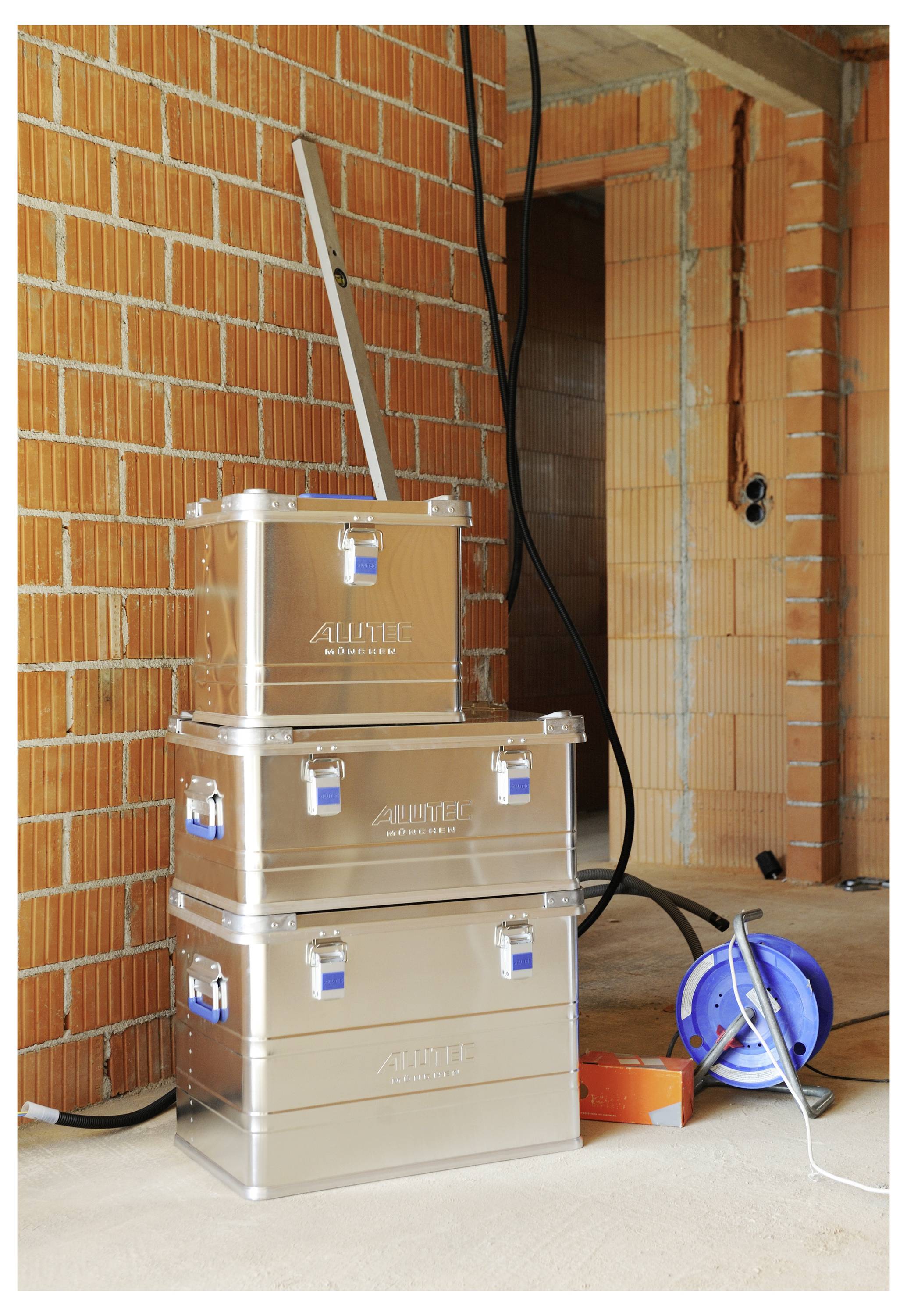 'Three stacked metal storage boxes with handles and latches, located in a partially constructed room with exposed brick walls and wiring.'