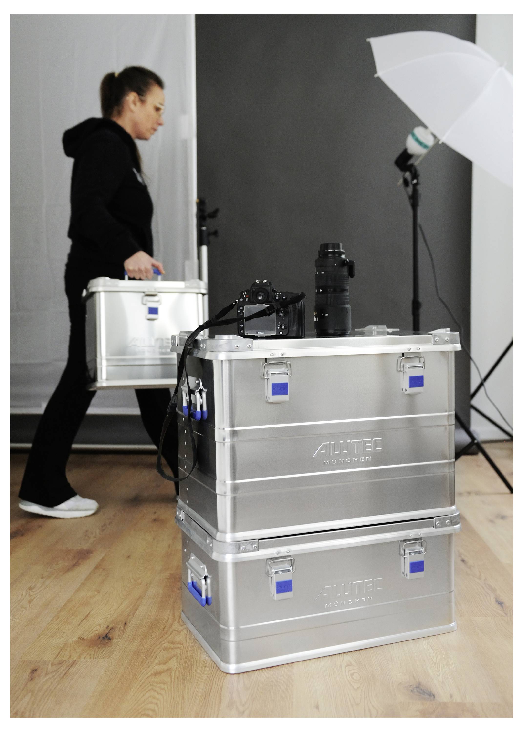 'A woman carrying a silver case walks past stacked cases and photography equipment in a studio setting.'