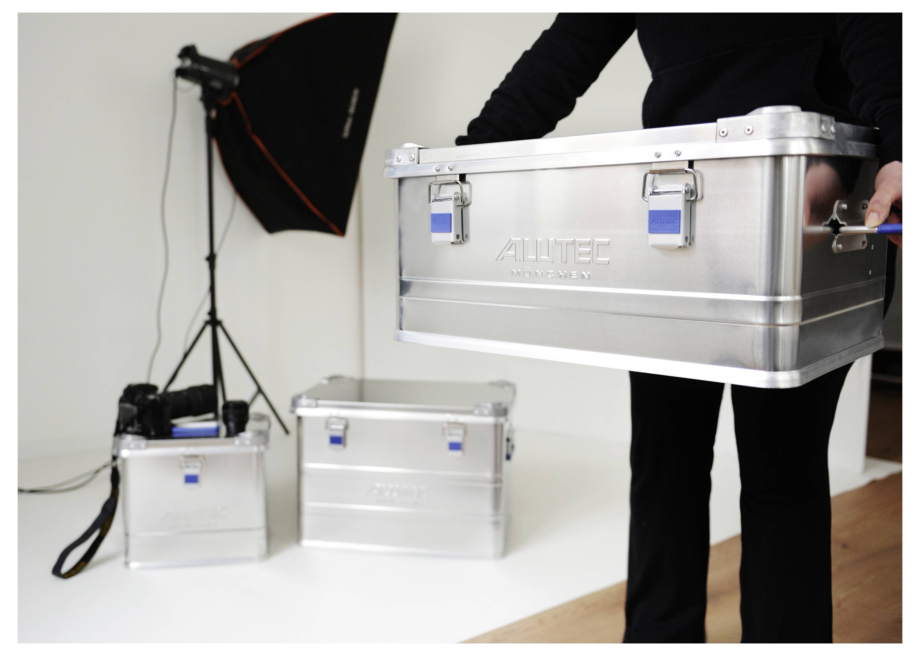 'A person carries a silver metallic storage case in a studio setting. Two similar cases and photography equipment are visible in the background.'
