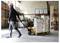 A worker in a warehouse pulls a pallet jack loaded with stacked metal boxes. Shelves with additional boxes are in the background.