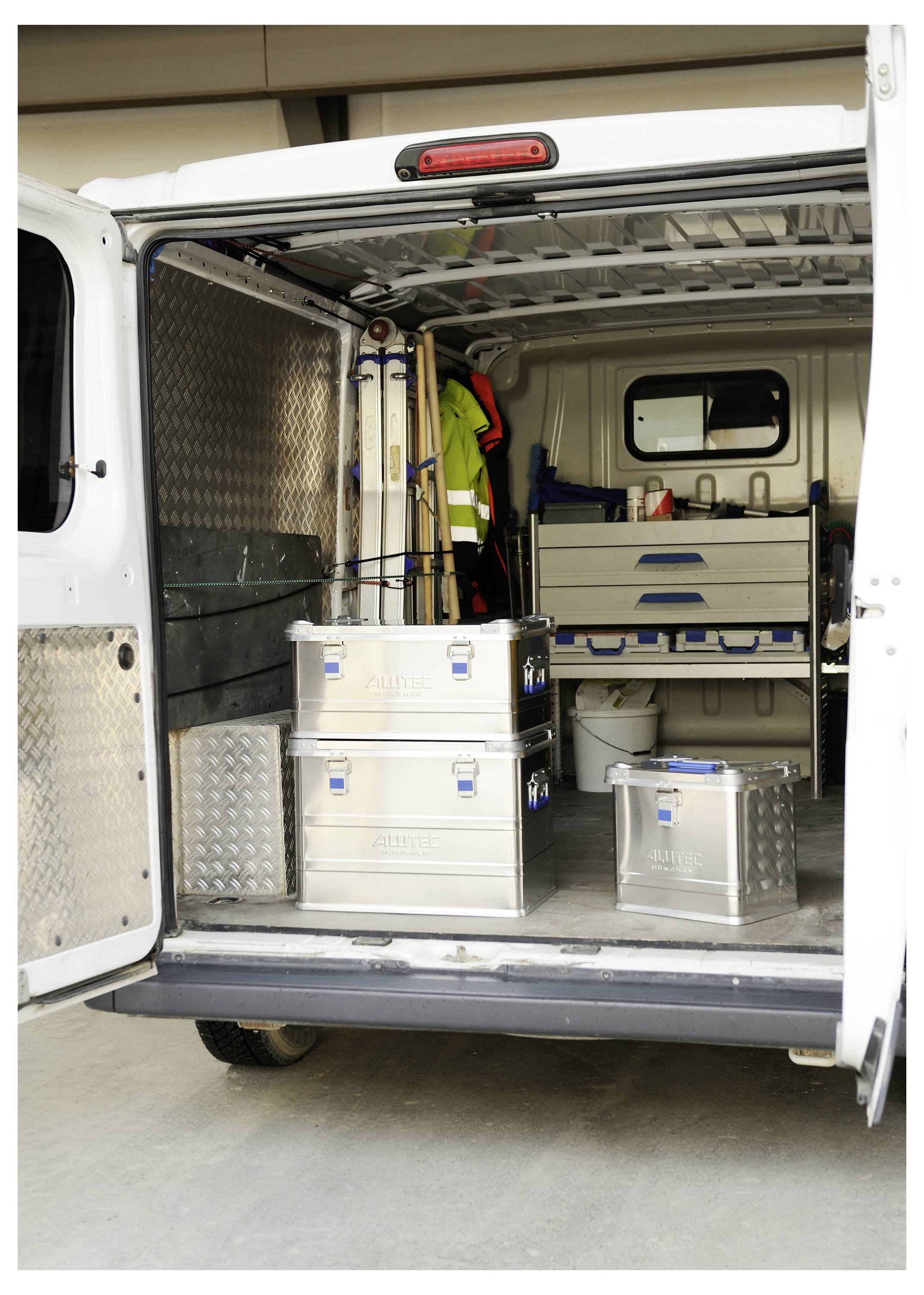 The back of a utility van is open, showing organized metal storage boxes, tools, and equipment inside.