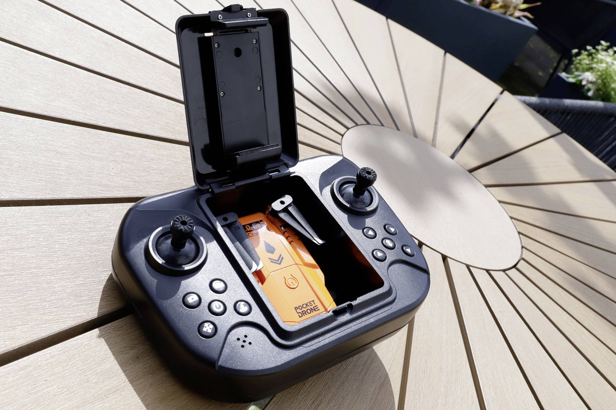 A drone remote control lies on a table. The top lid is open, revealing an orange compartment inside.