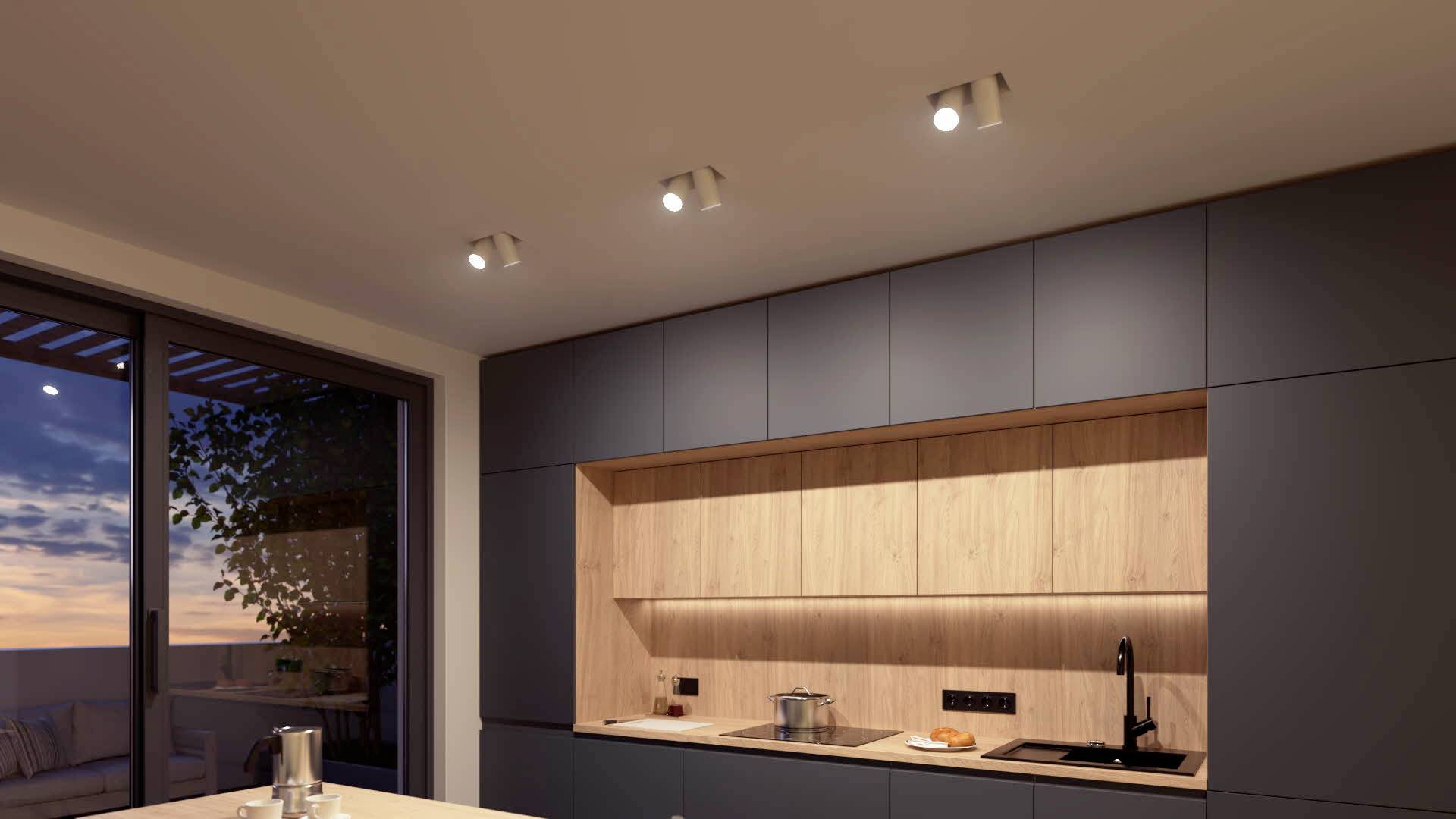 'Modern kitchen at sunset with built-in lighting, dark cabinets and a central worktop displaying a pot and fruit.'