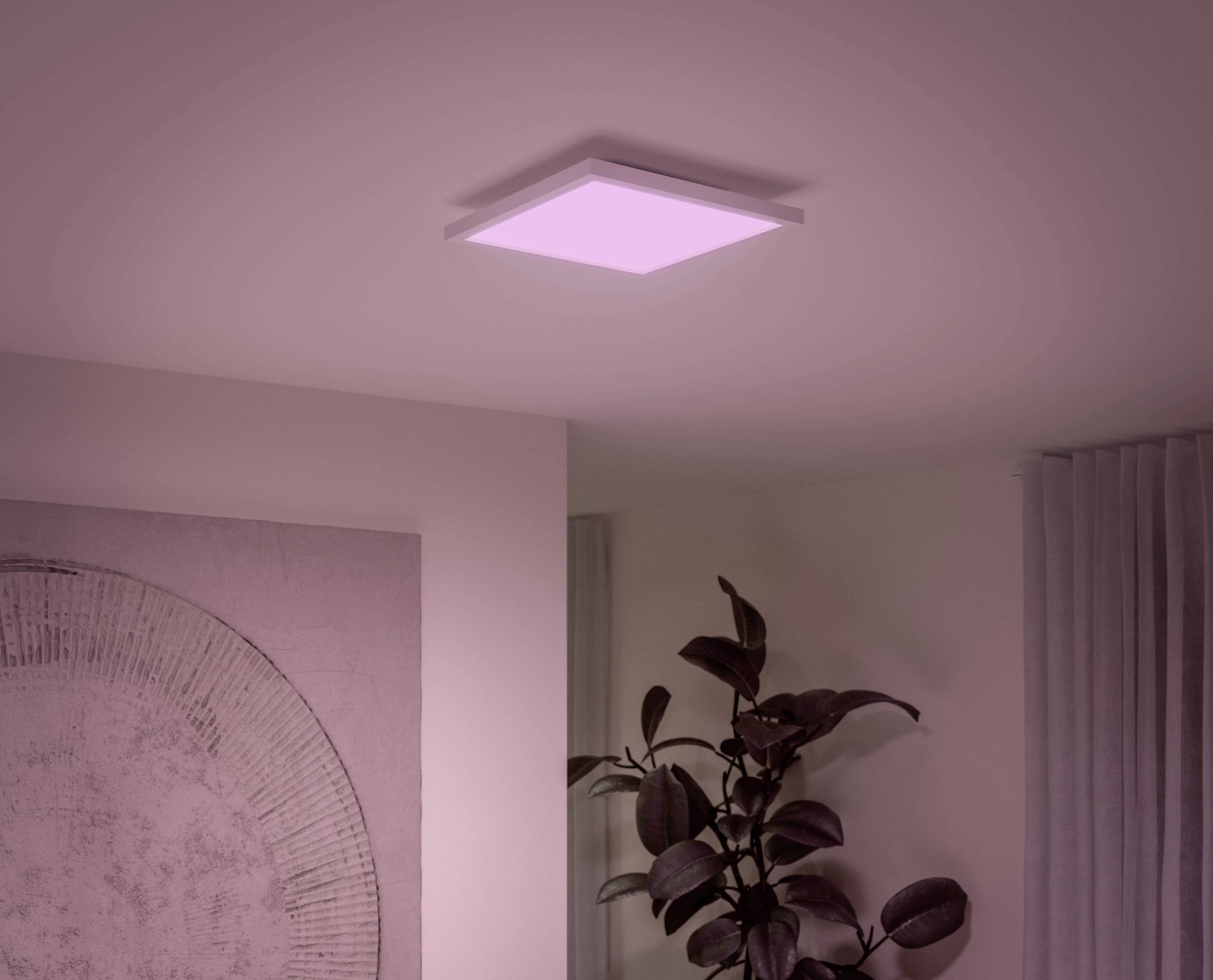 A square ceiling light emitting soft pink light illuminates a room ceiling. A plant stands beside it.