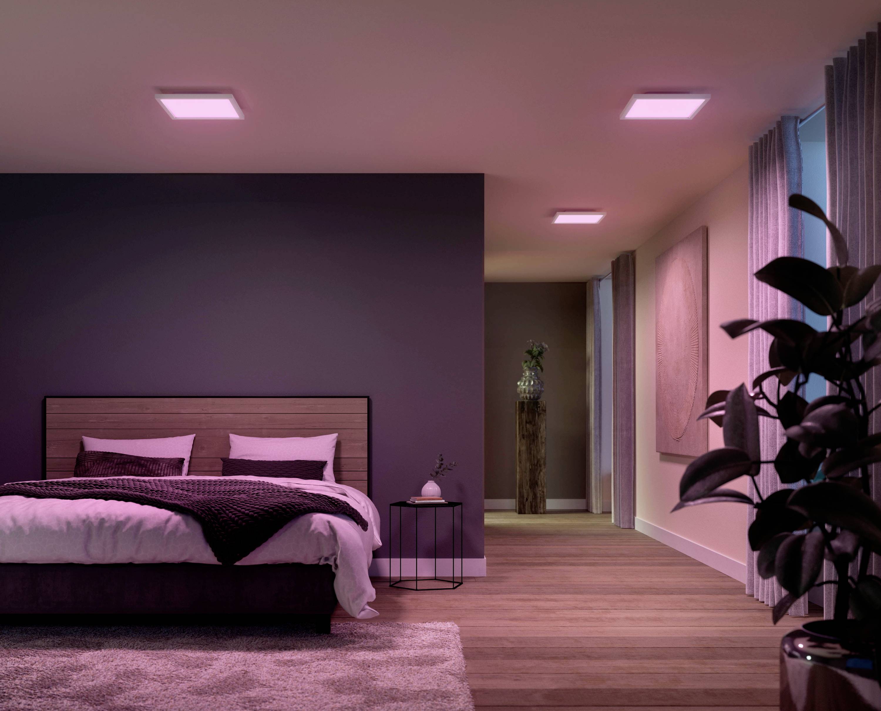 A modern furnished bedroom with illuminated ceiling light. A large bed stands to the left next to a small round table with a candle.