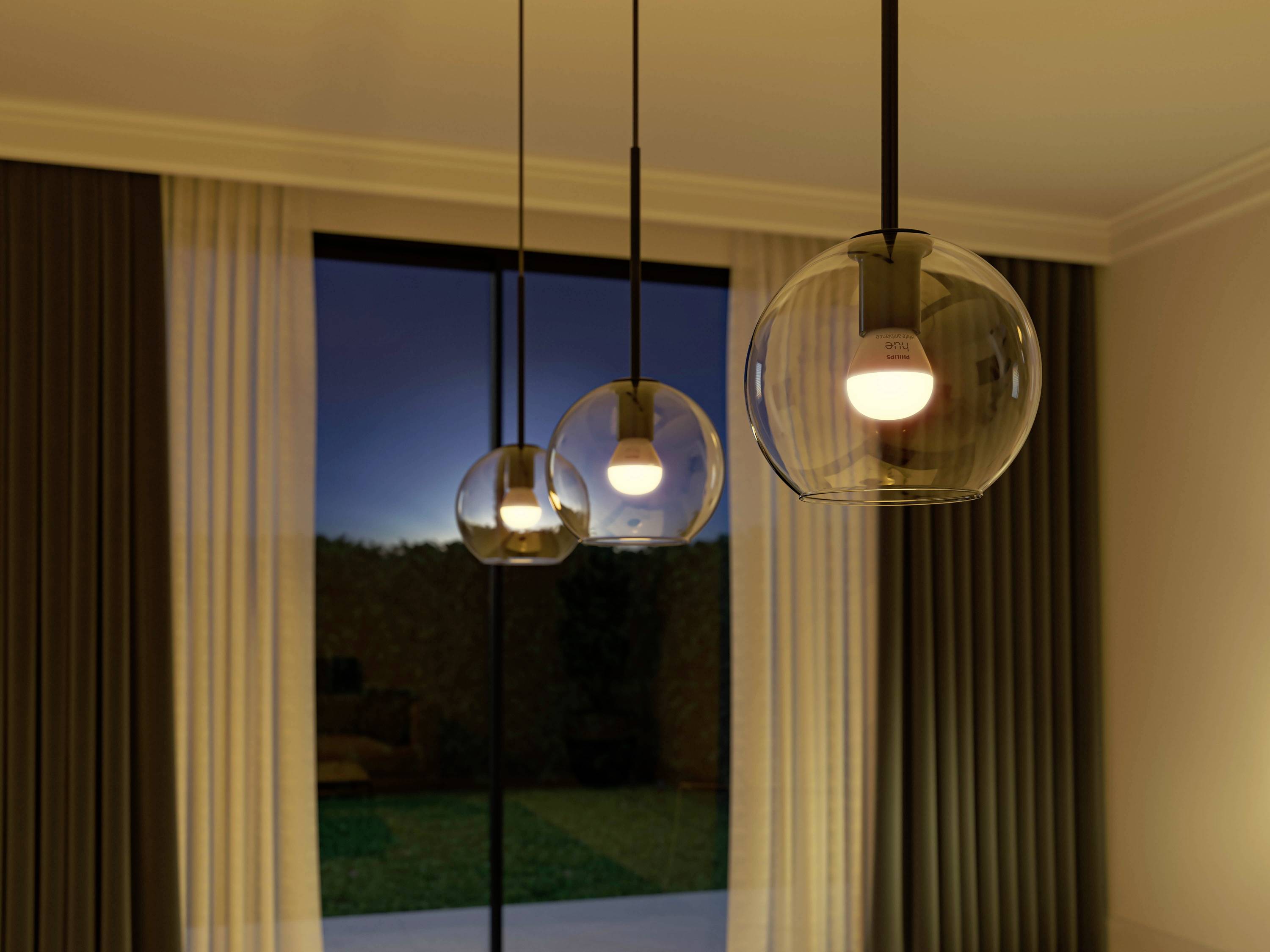 Three modern pendant lights hang from the ceiling in front of a large window with curtains. It is evening, and it is dark outside.